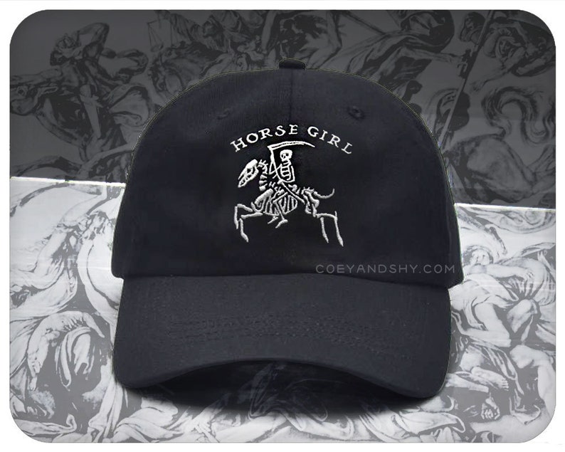 May include: Black baseball cap with a white embroidered design of a skeleton riding a horse. The text "HORSE GIRL" is above the design. The website "COEYANDSHY.COM" is printed on the back of the cap.