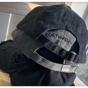 May include: Black baseball cap with a distressed look and the text "COEY and SHY" embroidered on the back.