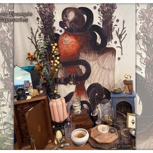 May include: A tapestry featuring a bird with a snake wrapped around it, surrounded by floral and botanical elements. The tapestry is hanging on a wall with a variety of decorative objects in front of it, including a small wooden cabinet, a lamp, and a glass jar. The text "Photo Example of Tapestries" is visible at the top of the image.