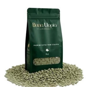 May include: A dark green stand-up pouch of Buna Utopia premium coffee from Ethiopia, featuring a clear window displaying raw green coffee beans. The bag is surrounded by a pile of unroasted coffee beans, with the text Guji printed below.
