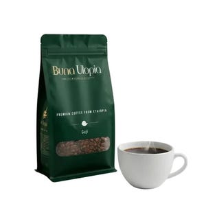 May include: A dark green coffee bag with the text Buna Utopia and Premium Coffee From Ethiopia Guji printed on the front, featuring a clear window showing roasted coffee beans, accompanied by a white ceramic mug filled with steaming black coffee.