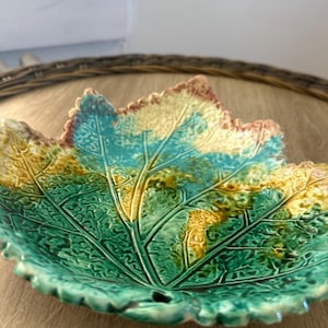 May include: A ceramic bowl shaped like a large leaf with a glossy finish. The surface features a textured vein pattern and a color palette of vibrant turquoise, deep green, and warm yellow, with brown edges along the serrated leaf border.
