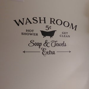 Peut inclure: Une affiche vintage noir et blanc qui dit "WASH ROOM 5&cent; HOT SHOWER GET CLEAN Soap & Towels -Extra-" avec une silhouette de baignoire. L'affiche est sur un mur blanc avec deux &eacute;tag&egrave;res en bois avec des supports en m&eacute;tal noir. Les &eacute;tag&egrave;res sont d&eacute;cor&eacute;es d'un pichet blanc, d'une bouteille en verre, d'un panier et d'un bol en c&eacute;ramique blanc avec des fleurs blanches.