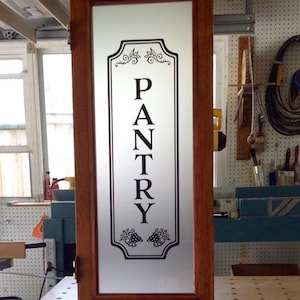 May include: A wooden door with a frosted glass panel featuring a black vinyl decal that reads "PANTRY" with a grapevine design at the bottom.