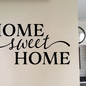 May include: Black and white vinyl wall decal with the text "Home Sweet Home" in a cursive font. The decal is applied to a white wall in a kitchen setting.