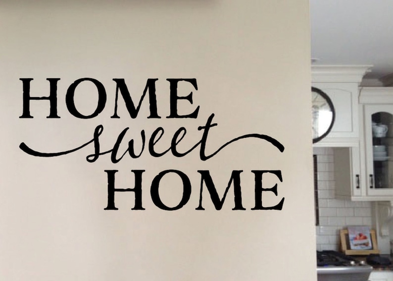 May include: Black and white vinyl wall decal with the text "Home Sweet Home" in a cursive font. The decal is applied to a white wall in a kitchen setting.
