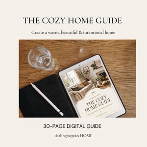 May include: A digital tablet displaying a 30-page digital guide titled THE COZY HOME GUIDE, featuring a white stylus pen on a black case, a clear glass, and text reading Create a warm, beautiful & intentional home and darlinghappies HOME.