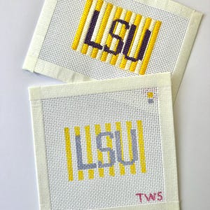 May include: Two square needlepoint canvases featuring the letters LSU in purple stitching over vertical yellow stripes. The bottom canvas includes the letters TWS in pink in the lower right corner and a small yellow and purple square icon.
