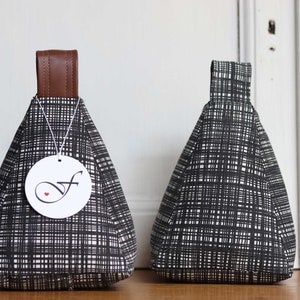 Könnte beinhalten: Zwei Türstopper mit einem schwarz-weißen Karomuster. Jeder Türstopper hat einen braunen Ledergriff und ein weißes Etikett mit einem stilisierten "f" und einem roten Herz. Die Türstopper sind dreieckig geformt.