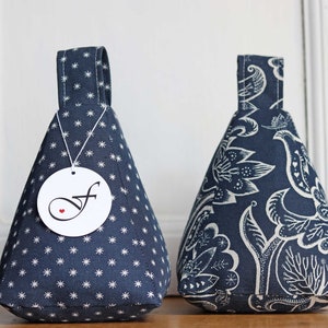 Könnte beinhalten: Zwei türstopper aus marineblauem Stoff. Einer hat ein weißes Sternmuster, der andere ein weißes Blumenmuster. Jeder hat eine Schlaufengriff und ein Etikett mit einem stilisierten "f" und einem Herzen.