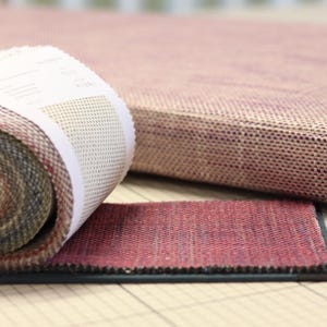 Könnte beinhalten: Stoffmuster in verschiedenen Farben und Texturen, darunter eine gerollte Probe und ein flaches Muster. Im Hintergrund befindet sich ein größeres Polsterteil. Die Stoffe sind wahrscheinlich für Polster oder Heimdekoration bestimmt.