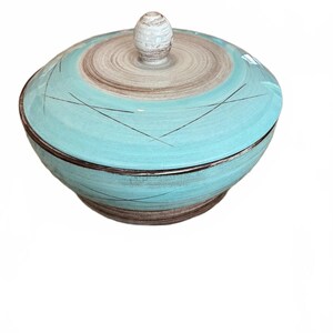 May include: A round ceramic lidded bowl featuring a vibrant turquoise glaze with brown brushstroke accents. The lid has a central knob and a circular pattern, while the bowl body displays thin, dark, intersecting lines across the surface.