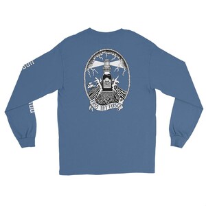 Puede incluir: Una camiseta azul de manga larga con un gráfico en la espalda de un faro con forma de botella con una calavera y tibias cruzadas, rodeado de olas, rayos y un borde de cuerda. Una cinta en la parte inferior dice "PASS THY POISON."