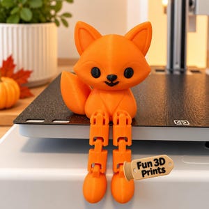 May include: A bright orange 3D printed fox figurine with a smooth finish, large pointed ears, and black eyes and nose. The fox has articulated, dangling legs and a bushy tail. A small beige tag attached to one leg features the text Fun 3D Prints.