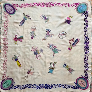 May include: A square cream-colored silk scarf featuring a border of pink and purple ribbons. The center is decorated with various illustrations of corsets, flowers, and fans. Four circular frames in the corners contain the years 1901, 1984, 1910, and 1960.