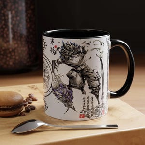 May include: A white ceramic mug with a black interior and handle, featuring a black and white ink-style illustration of an anime character with spiky hair and a dragon-like creature, accompanied by Japanese kanji text and decorative circular patterns.
