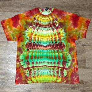 May include: A short-sleeve t-shirt featuring a vibrant tie-dye pattern with a symmetrical, vertical design in shades of bright yellow, turquoise, orange, and deep red. The center displays a repeating, intricate, organic, and web-like motif.