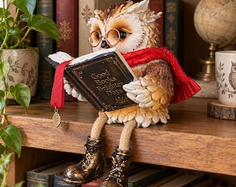 May include: A brown and white owl figurine wearing gold-rimmed glasses and a red scarf, sitting and reading an open book with the text Good Books Brighter Days. The owl has dangling legs with brown boots and a red bookmark with a gold leaf charm.