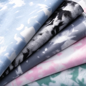 May include: A stack of folded fabric pieces featuring a tie-dye pattern. The layers display various color combinations including light blue and white, black and white, grey and white, pink and white, and green and white with a visible weave.