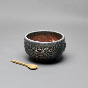 May include: A white ceramic mug with a black handle and the text "But First, Coffee" in a bold, black font. The mug is set against a blurred background, highlighting its simple design.