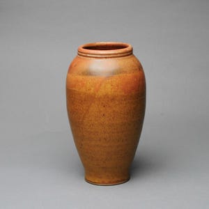 May include: A handcrafted, ceramic vase with a wide opening and a rounded body. The vase has a speckled, earthy brown and orange glaze. The vase is approximately 10 inches tall.
