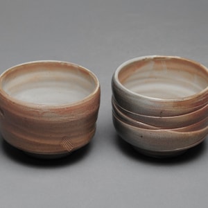 May include: Two ceramic bowls with a light brown glaze. The bowls have a slightly textured surface and are slightly different in size.