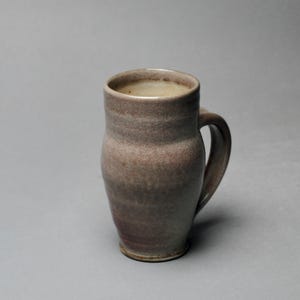 May include: A ceramic mug with a light purple glaze and a rounded body. The mug has a handle and a slightly flared rim.