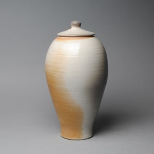 May include: A white ceramic jar with a lid, featuring a brown glaze that fades to white. The jar has a rounded body and a narrow neck.