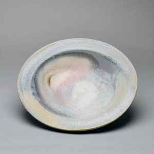 May include: A ceramic bowl with a wide rim and a shallow interior. The bowl features a blend of colors, including white, pink, blue, and yellow, creating a soft, watercolor-like effect. The bowl's design is simple and elegant, suitable for serving food or as a decorative piece.
