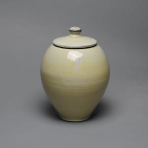 May include: A yellow ceramic jar with a lid. The jar has a smooth, glossy finish and a rounded shape.