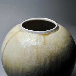 以下が含まれることがあります： 薄い茶色の釉薬がかかった丸い陶器の花瓶。花瓶は白い縁取りがあり、表面はわずかにざらざらしている。