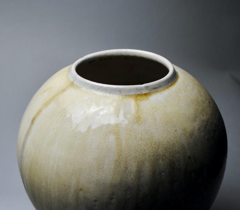 以下が含まれることがあります： 薄い茶色の釉薬がかかった丸い陶器の花瓶。花瓶は白い縁取りがあり、表面はわずかにざらざらしている。