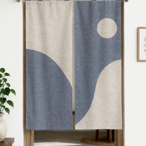 Könnte beinhalten: Ein Paar rechteckige Türvorhänge aus Stoff mit einem zweifarbigen Design in Beige und Staubblau. Die Vorhänge hängen an einer Holzstange mit Stoffschlaufen und zeigen ein geschwungenes abstraktes Muster mit einem Kreis auf der rechten Seite.