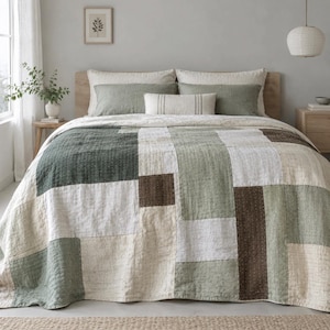 May include: A patchwork quilt featuring rectangular blocks in shades of sage green, cream, and dark brown. The quilt has visible stitching details and covers a bed with two large sage green pillows and a smaller cream lumbar pillow with stripes.