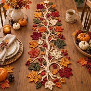 May include: A long, crocheted table runner featuring a central vine design with intricate, multi-colored maple leaves in shades of red, orange, yellow, and green, accented with small clusters of red and yellow berries throughout the length.