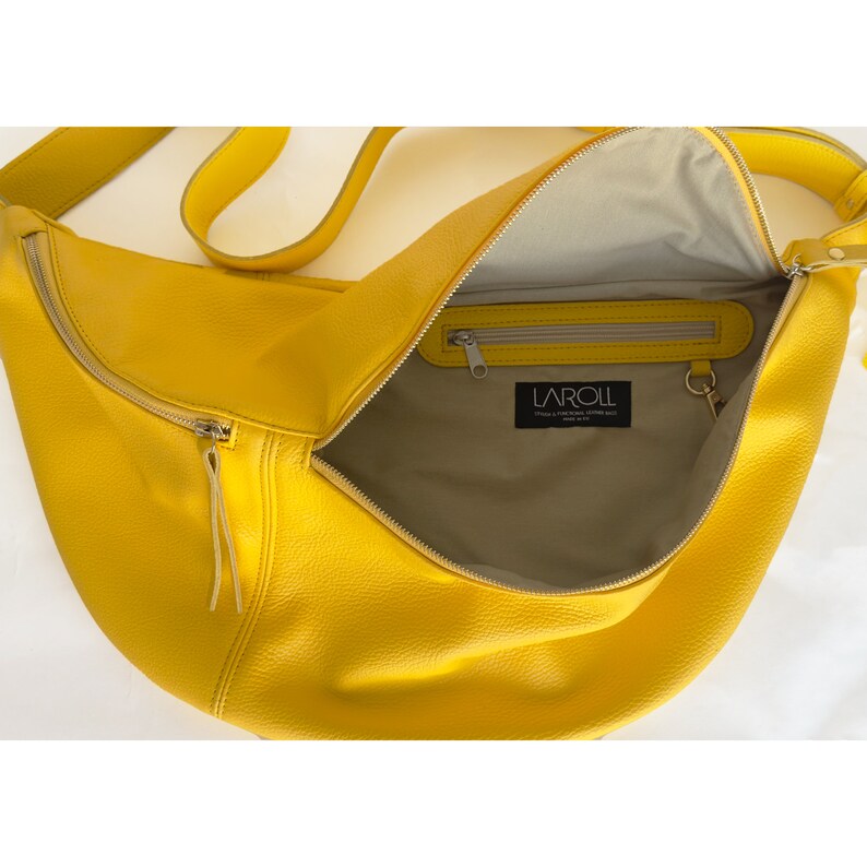 May include: A bright yellow leather crossbody bag with a zipper closure and a small interior pocket. The bag is open and the interior lining is a light beige color. The brand name "LAROLL" is printed on a black label inside the bag.