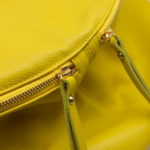 May include: A bright yellow leather bag with a gold zipper and two leather straps.