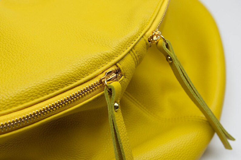 May include: A bright yellow leather bag with a gold zipper and two leather straps.