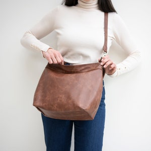 May include: A brown leather shoulder bag with a long strap. The bag is open and the inside is visible.