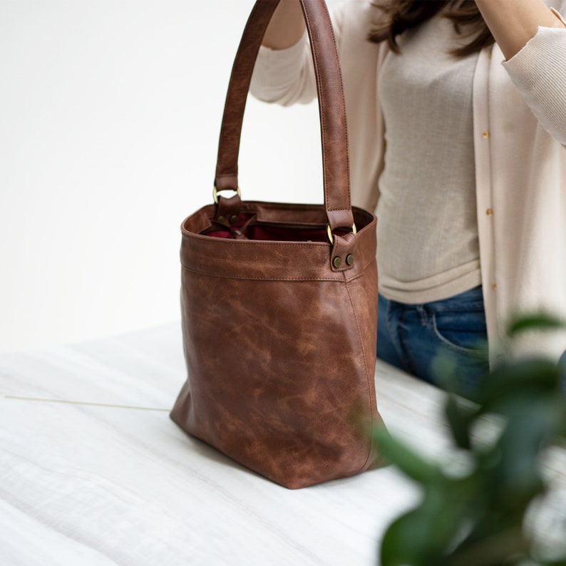 May include: A brown leather tote bag with a top zipper closure and two top handles. The bag has a distressed look and is made of a soft, supple leather.