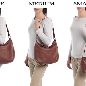 May include: A brown leather hobo bag shown in three sizes labeled LARGE, MEDIUM, and SMALL. The bag features a slouchy, rounded silhouette, a single shoulder strap attached with metal rings, and a top zipper closure. The leather has a smooth finish.