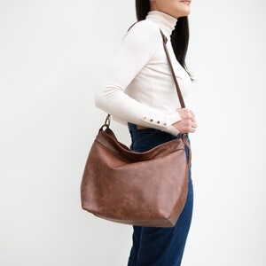 May include: A brown leather shoulder bag with a long strap. The bag has a slouchy, casual style.
