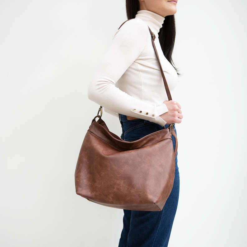 May include: A brown leather shoulder bag with a long strap. The bag has a slouchy, casual style.