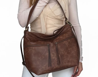 May include: A brown leather satchel handbag with a long adjustable strap. The bag has multiple zippered pockets and a tassel detail.