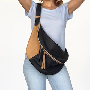 Könnte beinhalten: Eine schwarze und braune Leder-Umhängetasche mit einem langen Riemen. Die Tasche hat einen Reißverschluss und eine Klappe.