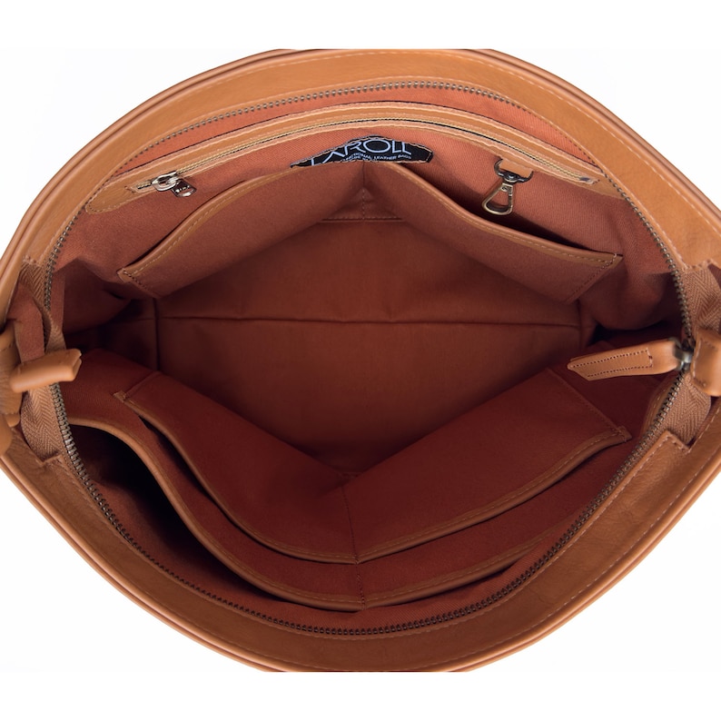 May include: The interior of a tan leather bag featuring a brown fabric lining, a zippered pocket, a metal key clip, and multiple open slip pockets. A black label with the white text TAROLL is stitched near the top edge of the main compartment.