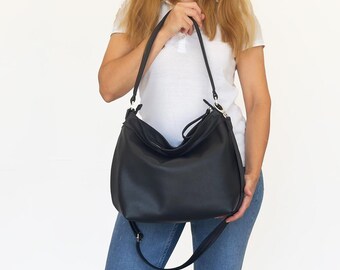 May include: A black leather shoulder bag with a long strap. The bag has a slouchy design and a zipper closure.