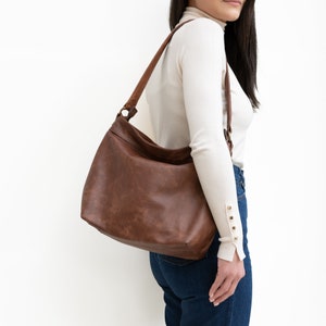 May include: A brown leather shoulder bag with a long strap. The bag has a flap closure and a buckle detail.