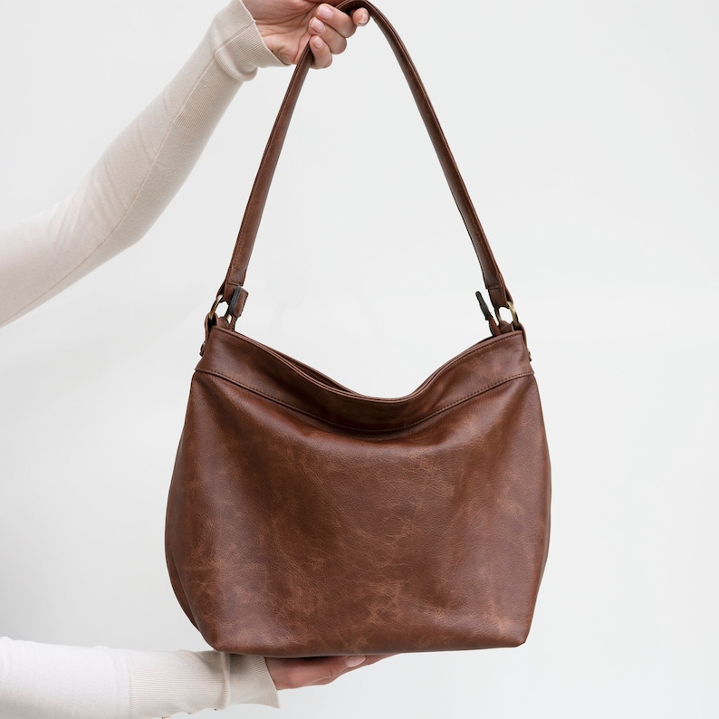 May include: A brown leather shoulder bag with a single strap. The bag has a flap closure and a gold-toned buckle.