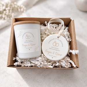 May include: A brown cardboard gift box containing a white candle with a bamboo lid and a round white ceramic ornament with a ribbon. Both items feature the text Congratulations On Your Engagement, Freya & Oliver, and 13.10.2027.